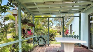 A covered patio area with a white table, surrounded by lush greenery and a wooden fence. - Perfect Fishing Holiday (Burrum Heads)