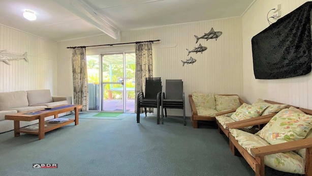 A living room with a sofa, a wooden coffee table, a TV stand, and a patterned sofa. - Perfect Fishing Holiday (Burrum Heads)