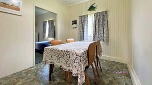 A dining area with a table covered by a lace tablecloth, wooden chairs, and a fish decoration on the wall. - Perfect Fishing Holiday (Burrum Heads)