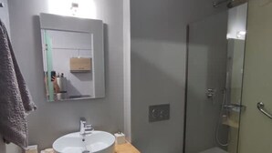 A modern bathroom with a round sink, a toilet, and a glass shower enclosure.