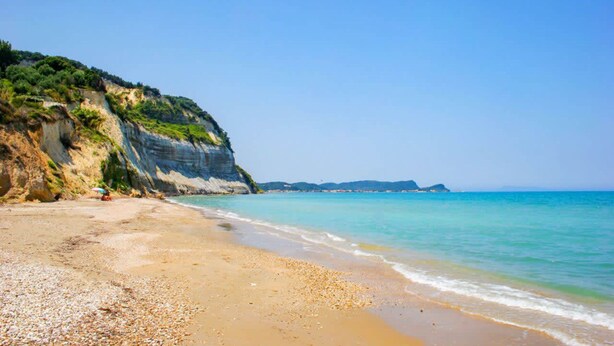 Une plage bordée d’une falaise rocheuse et baignée par une mer calme.