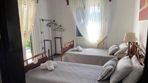 Une chambre avec deux lits, chacun recouvert d’une courtepointe et doté d’oreillers, une table de chevet avec une lampe, et une fenêtre ornée de rideaux légers.