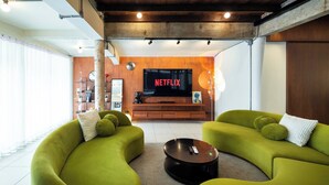 Ein modernes Wohnzimmer mit grünen Sofas, einem Couchtisch und einem großen Fernsehbildschirm, der 'NETFLIX' zeigt.