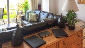 A living room with a leather sofa, a wooden coffee table with books and a lantern, and a potted plant. - 2 bedroom accommodation in St Dogmaels (St Dogmaels)