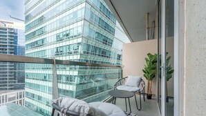 Ein Balkon mit Glasgeländer, zwei Korbstühle, ein kleiner Tisch und ein Blumentopf.