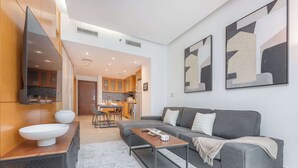 Ein modernes Wohnzimmer mit einem grauen Sofa, einem Couchtisch und einem großen Spiegel. Im Hintergrund ist eine Küche mit Holzschränken und einem Essbereich zu sehen.