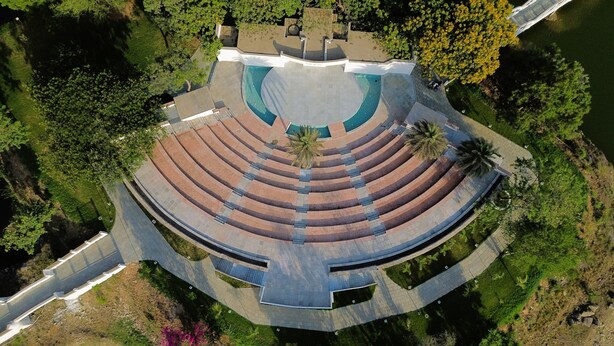 An aerial view of a circular amphitheater with tiered seating, surrounded by greenery and a body of water. - Praveg Rezort Kachigam (Daman)