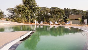 A swimming pool with lounge chairs and a wooden deck. - Praveg Rezort Kachigam (Daman)