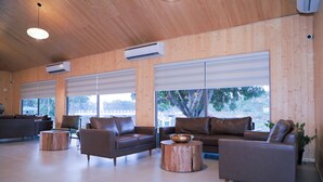 A spacious indoor area with wooden walls, large windows, and multiple seating arrangements including sofas and round tables. - Praveg Rezort Kachigam (Daman)