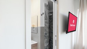 Ein Badezimmer mit Dusche, Waschbecken und Spiegel. Ein digitales Schild an der Wand zeigt den Schriftzug "barrooms".