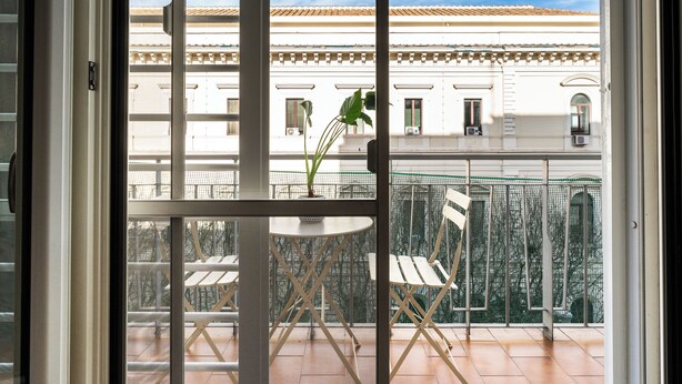 Ein Balkon mit Tisch und Stühlen, einem Blumentopf und Blick auf ein Gebäude mit Ziegeldach.