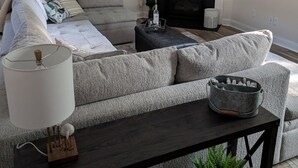 Un salon avec un canapé gris, une cheminée, un téléviseur à écran plat et un ventilateur de plafond.