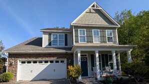 Une maison à deux étages avec un garage, une véranda et une pelouse bien entretenue.