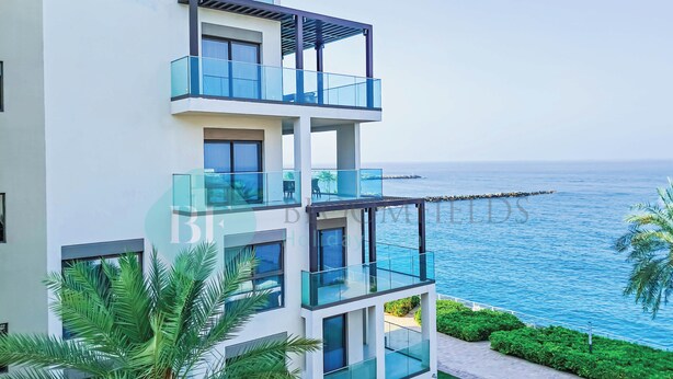Un immeuble moderne à plusieurs étages, doté de balcons en verre offrant une vue sur la côte.