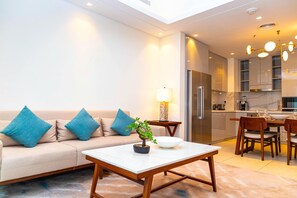 A modern living room with a sofa, a coffee table, and a dining area with chairs and a kitchen in the background. - Bloomfields 2BR Plus Maid Address Beach (Al Aqah)