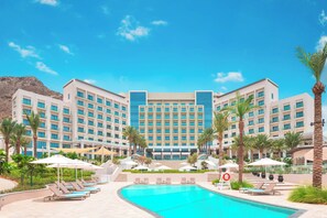 A hotel with a swimming pool, multiple balconies, and palm trees. - Bloomfields 2BR Plus Maid Address Beach (Al Aqah)