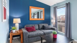 Een moderne woonkamer met een blauwe accentmuur, een grijze bank, een houten salontafel en een groot raam met gordijnen.