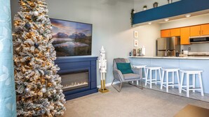 Een moderne woonkamer met een open haard, een kerstboom, een televisie en een keuken met oranje kastjes.