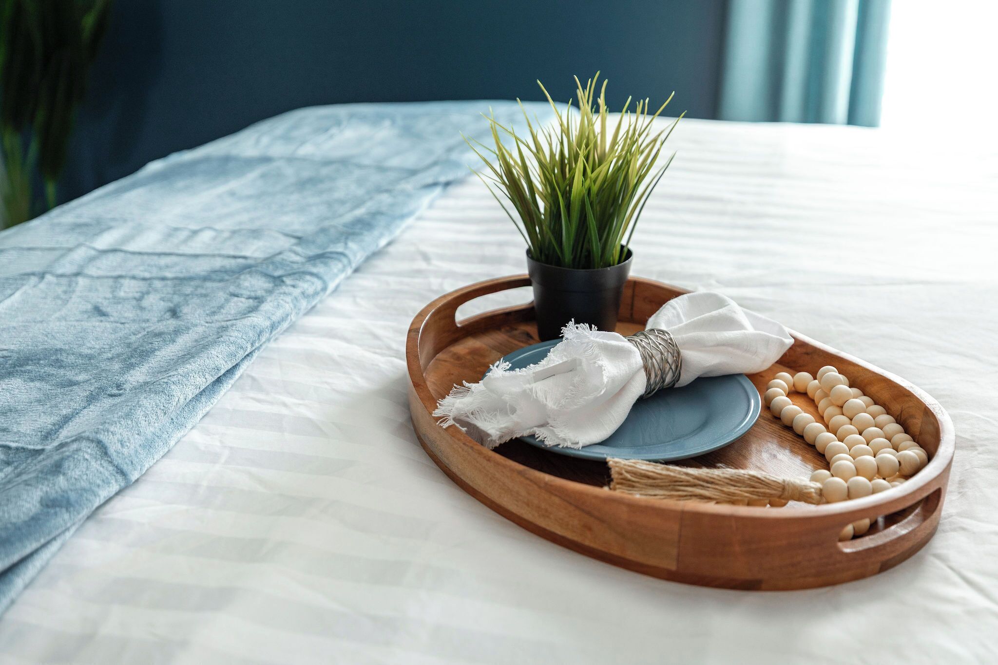 Un plateau en bois avec une plante, un tissu blanc et un ensemble d’objets ronds, le tout posé sur un lit recouvert d’un drap blanc et d’une couverture bleue.