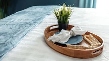 Een houten dienblad met een plant, een witte doek en een verzameling ronde voorwerpen op een bed met een witte lakenset en een blauwe deken.