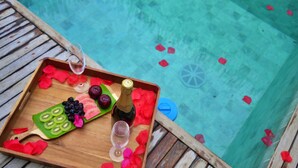 A wooden tray with a bottle of champagne, glasses, and fruit on a deck by a pool. - Oribá Chalé Boutique (Sao Miguel dos Milagres)