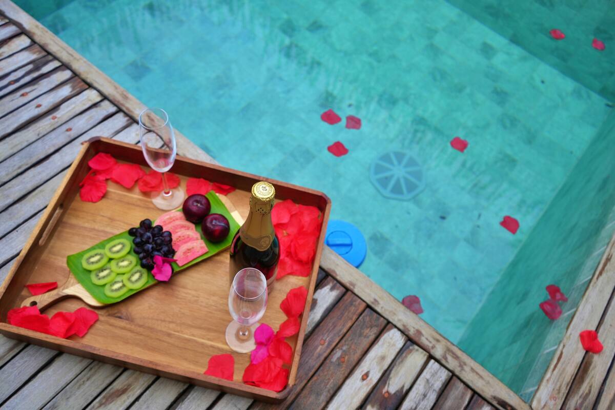 Ein hölzernes Tablett mit Champagner, Gläsern und Obst auf einer Poolterrasse.
