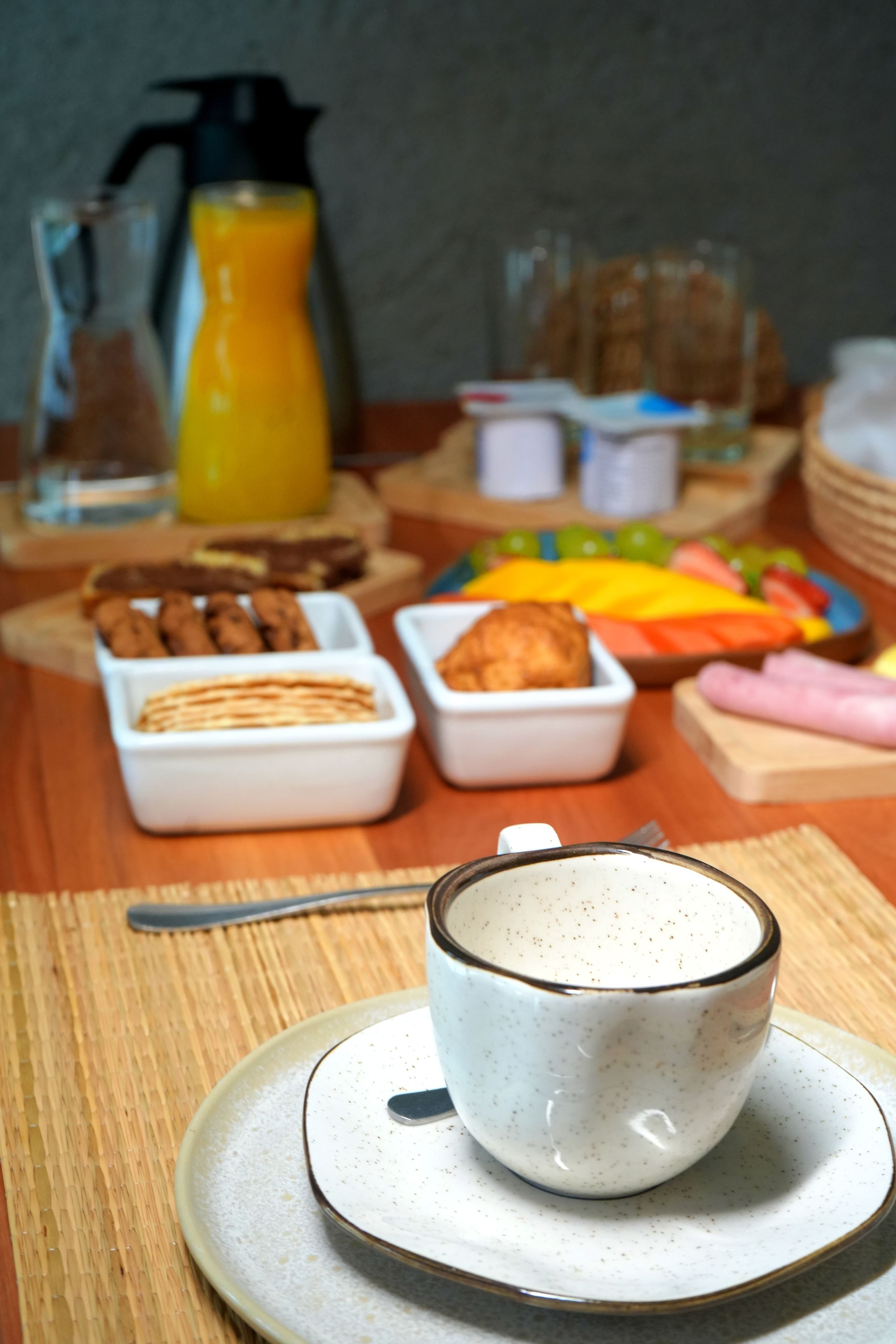 A breakfast setting with a cup of coffee, a glass of orange juice, and various pastries and snacks on a wooden table.