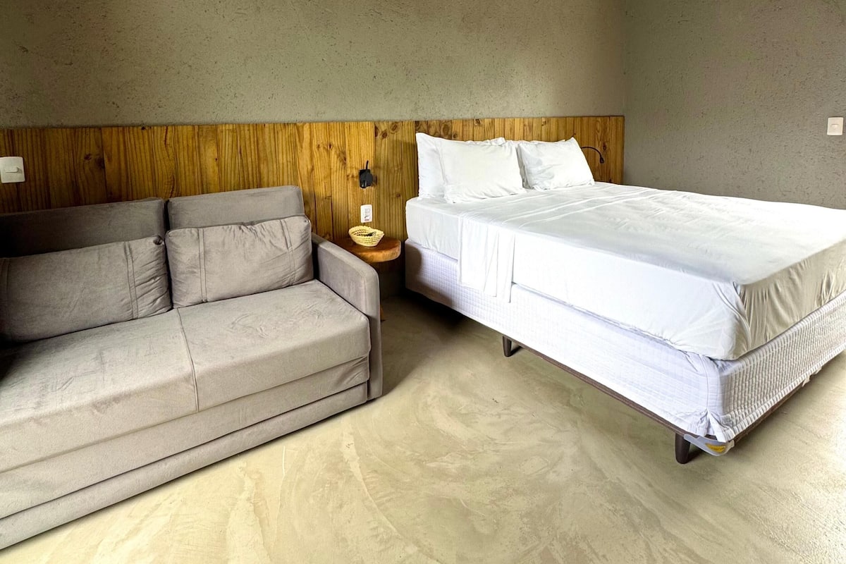 Ein Schlafzimmer mit einem hölzernen Kopfteil, einem Einzelbett, einem grauen Sofa und einem kleinen Nachttisch mit einer Lampe.
