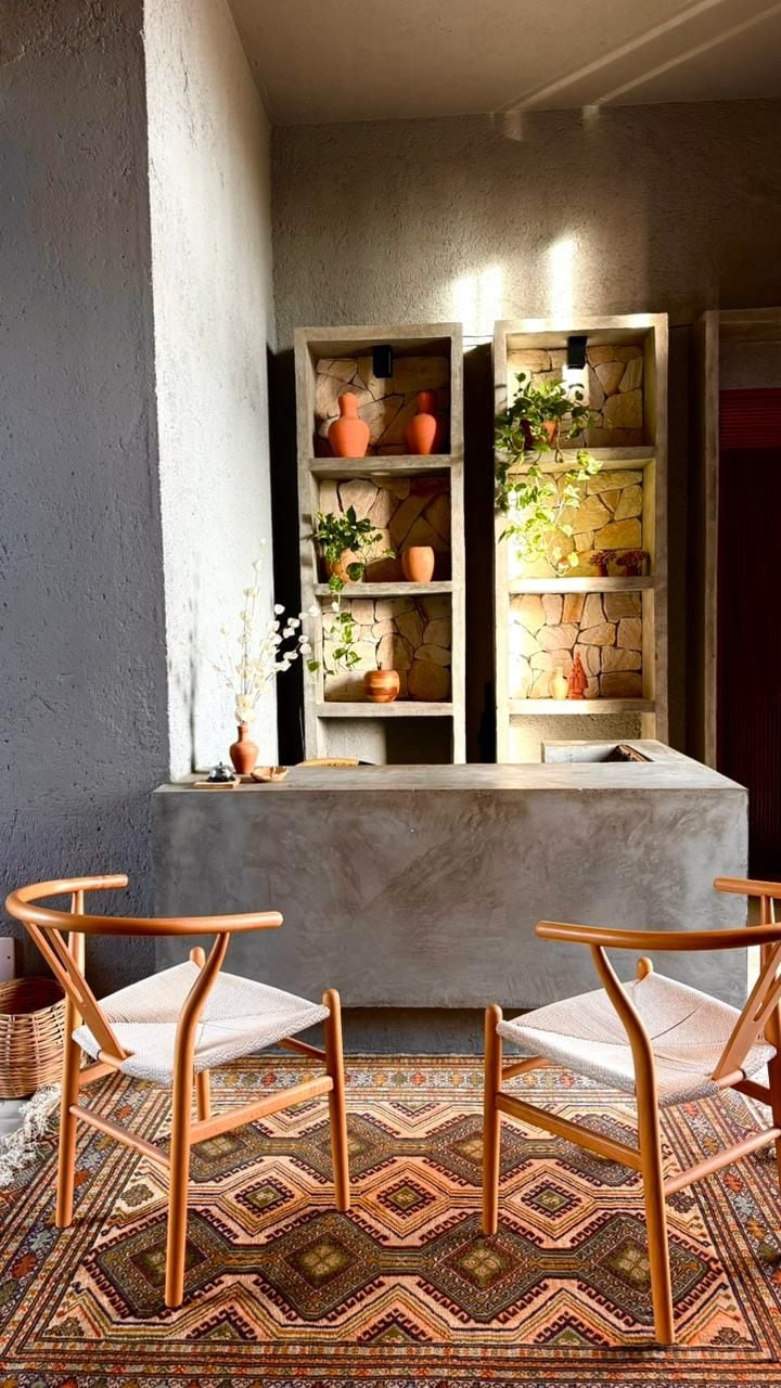 A room with a concrete bench, two wooden chairs, and a patterned rug.