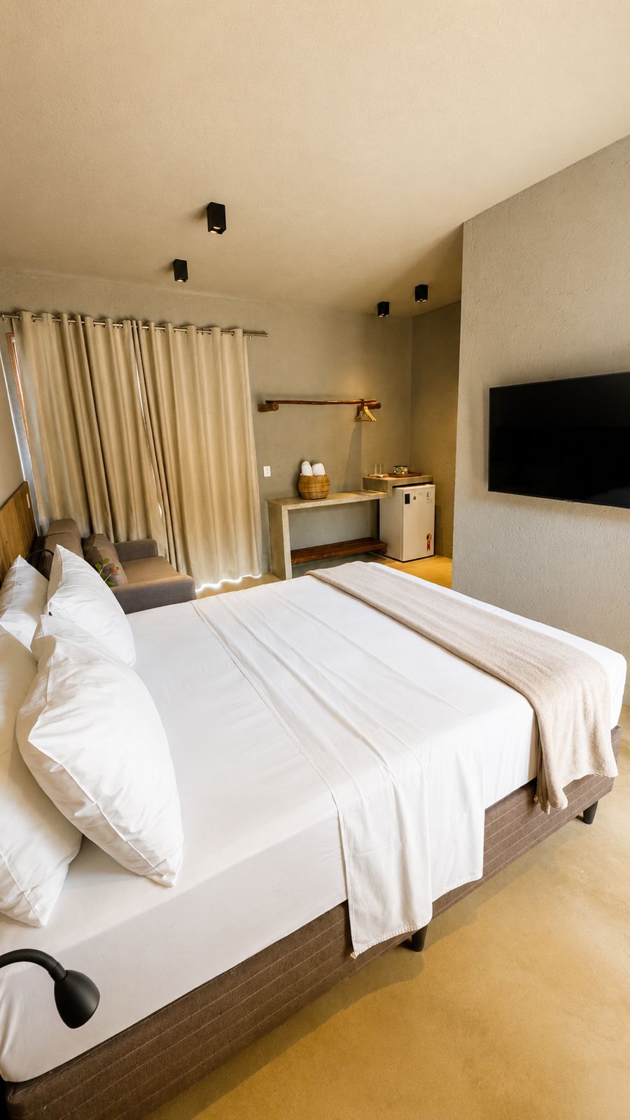 Une chambre d’hôtel avec un grand lit, un bureau avec une lampe, une télévision et une fenêtre avec des rideaux.