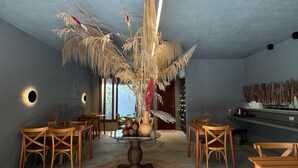 A modern interior with a central round table, wooden chairs, a vase with dried plants, and a wall-mounted light fixture. - Oribá Chalé Boutique (Sao Miguel dos Milagres)