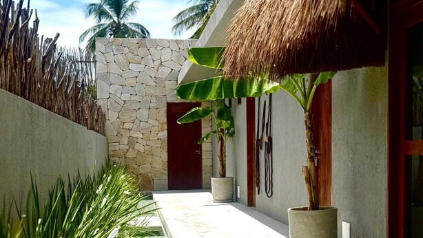 A modern building with a stone wall, a thatched roof, and a concrete pathway. - Oribá Chalé Boutique (Sao Miguel dos Milagres)