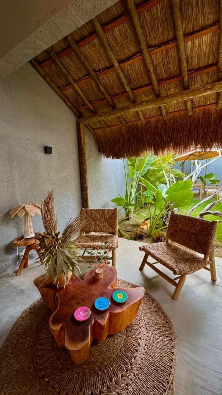 A covered outdoor seating area with woven chairs and a central table with a plant.