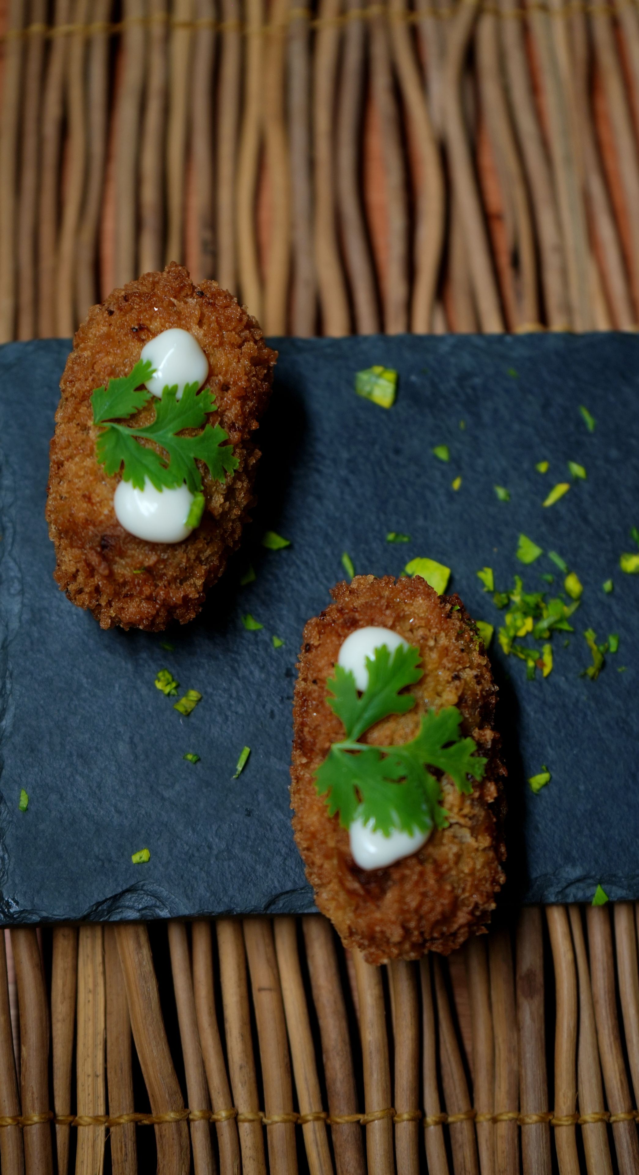 Två panerade och friterade rätter, serverade med en klick grädde och garnerade med ett blad på en skifferbricka.