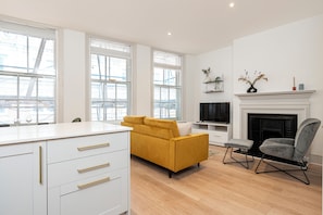 A modern living room with a yellow sofa, a grey armchair, and a fireplace. - JOIVY Stylish 1 bed flats in Soho (London)