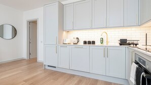 A modern kitchen with light grey cabinets, a wooden floor, and a built-in oven. - JOIVY Stylish 1 bed flats in Soho (London)