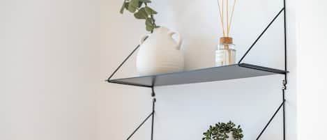 Una jarra de cerámica blanca sobre una estantería de metal negro con libros y una pequeña planta.