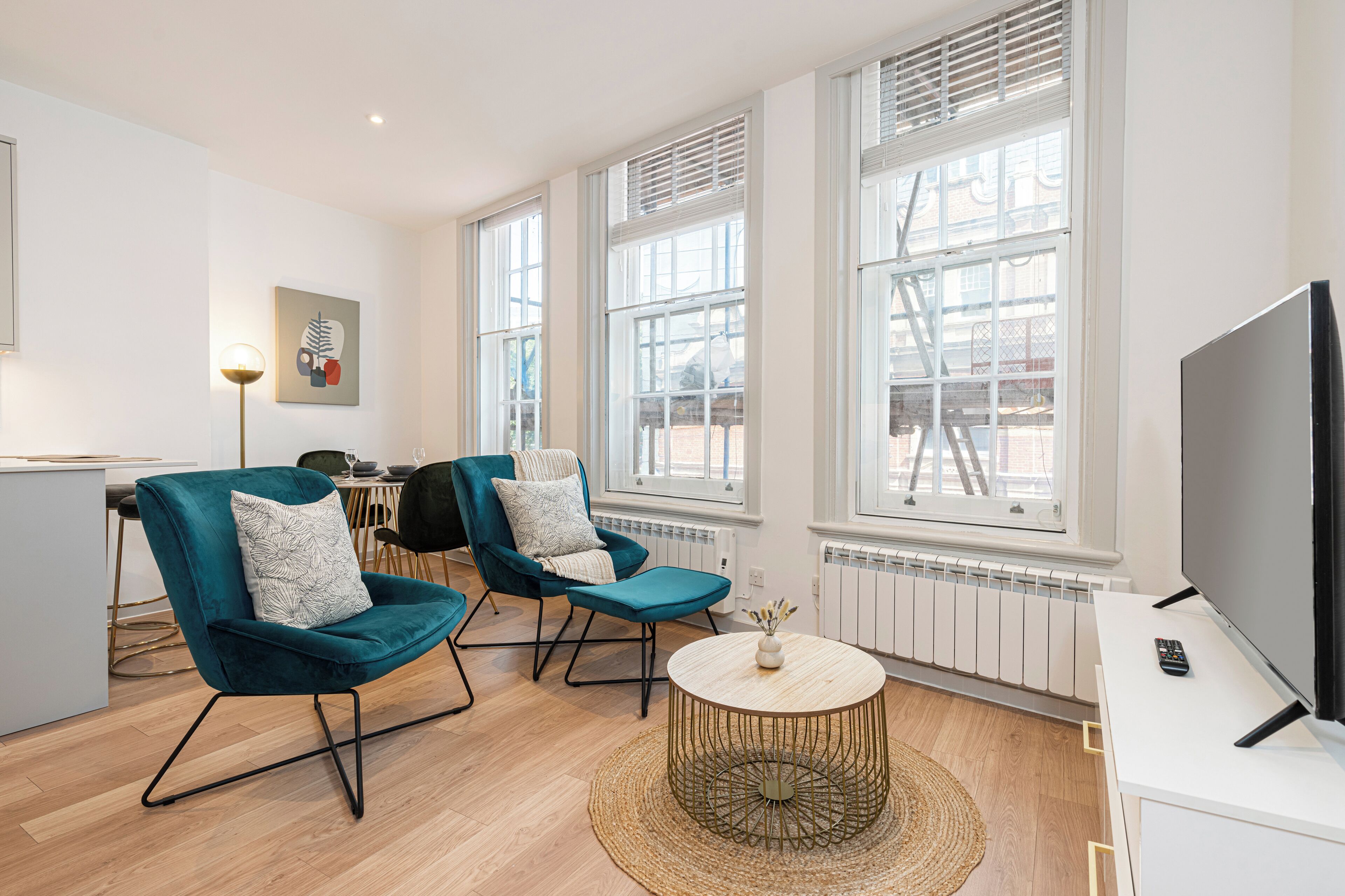Una sala moderna con dos sillones color turquesa, una mesa de centro redonda, un televisor de pantalla plana y ventanas grandes.
