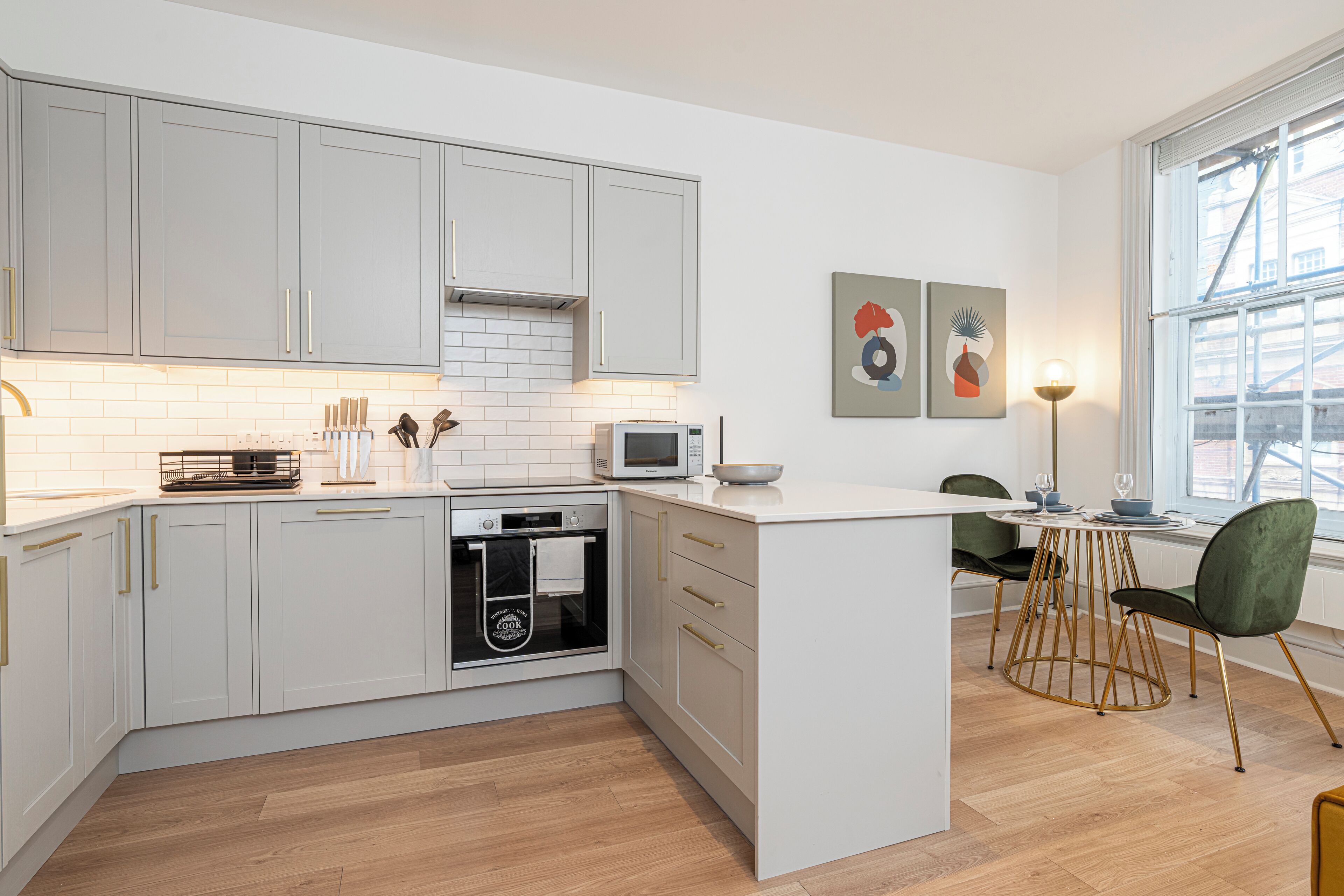 A modern kitchen with white cabinetry, a built-in oven, and a dining area with a round table and chairs.