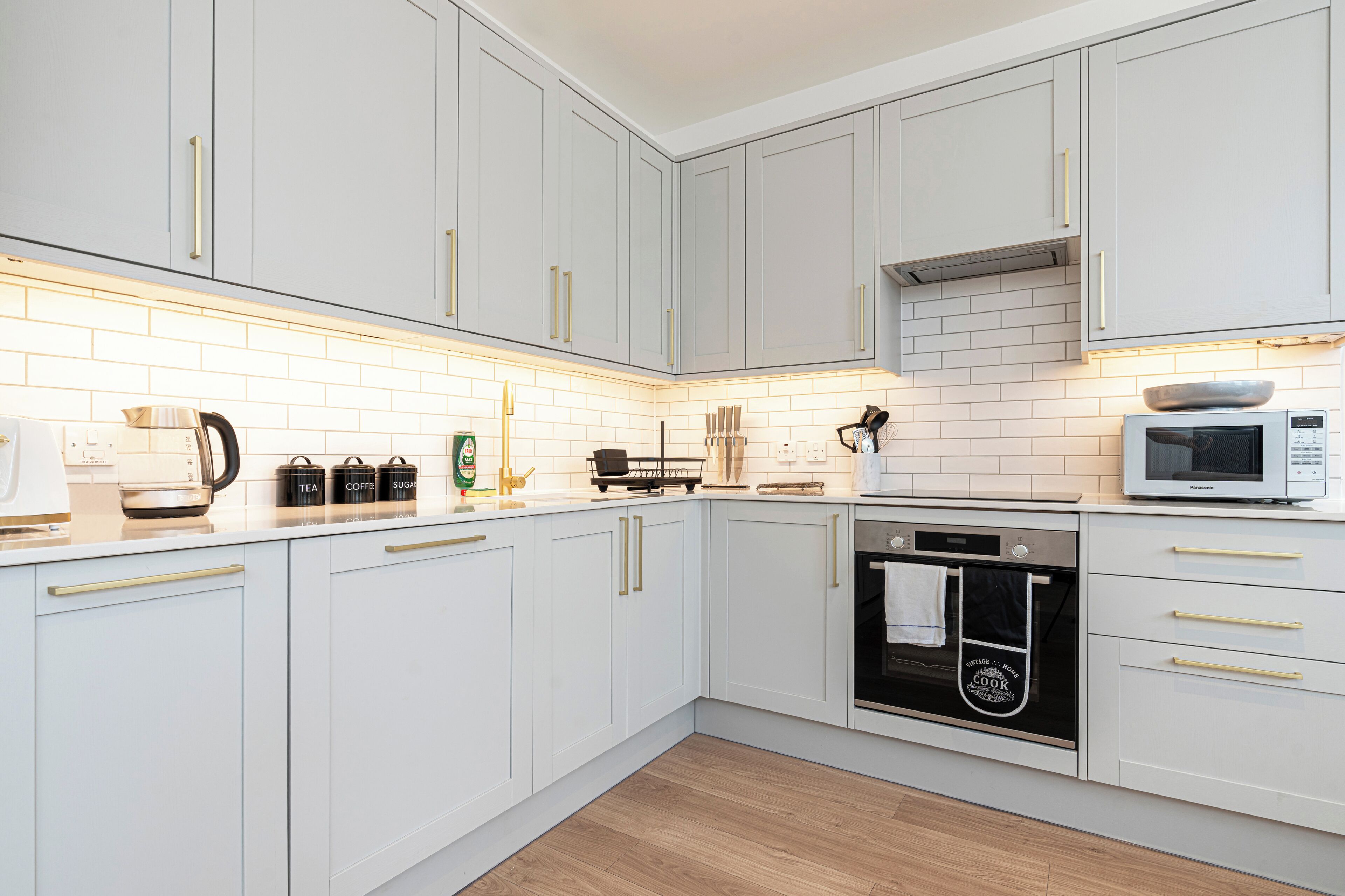 A modern kitchen with white cabinets, a microwave, an oven, and a coffee maker.