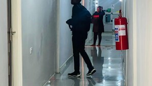 Un pasillo largo y estrecho con suelo de baldosas brillantes y paredes blancas. Un extintor rojo está sujeto a la pared.