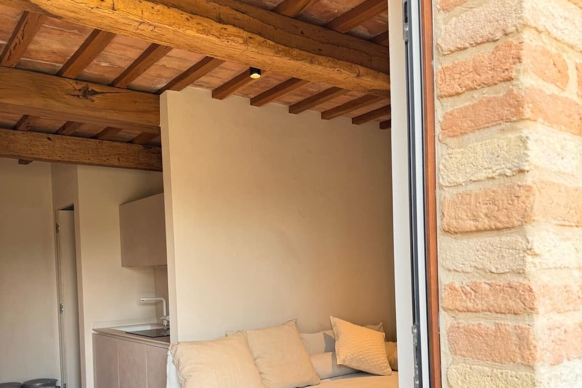 Una habitación acogedora con una cama, un pequeño rincón de cocina y suelo de baldosas de piedra.