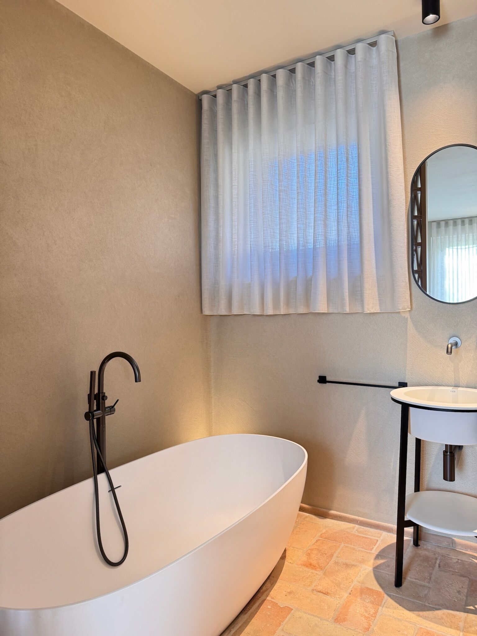A modern bathroom with a freestanding bathtub, a wall-mounted sink, and a window with curtains.