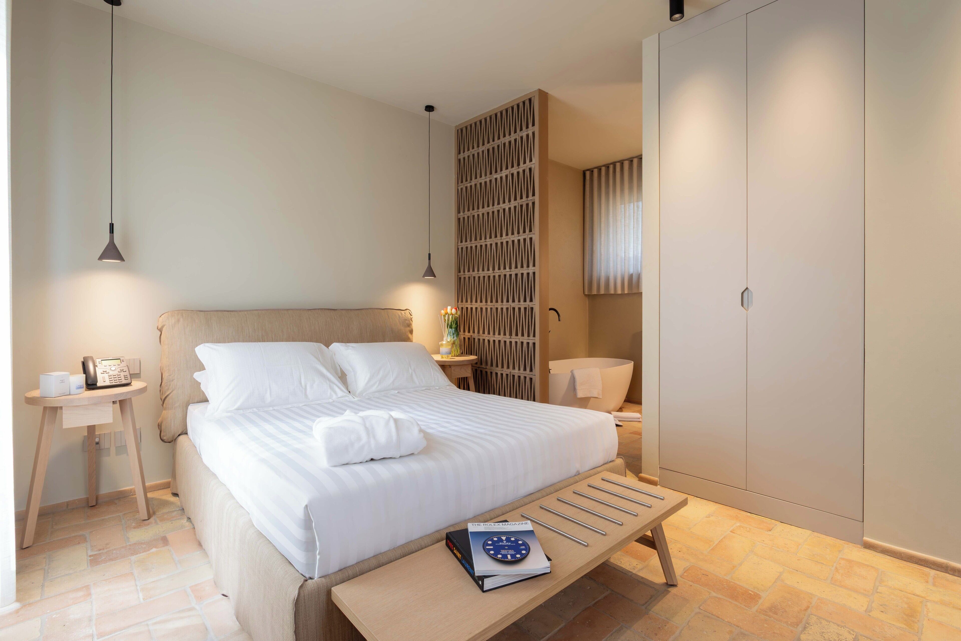 A neatly arranged bedroom with a bed, bedside tables, a nightstand, a bookshelf, and a wardrobe.