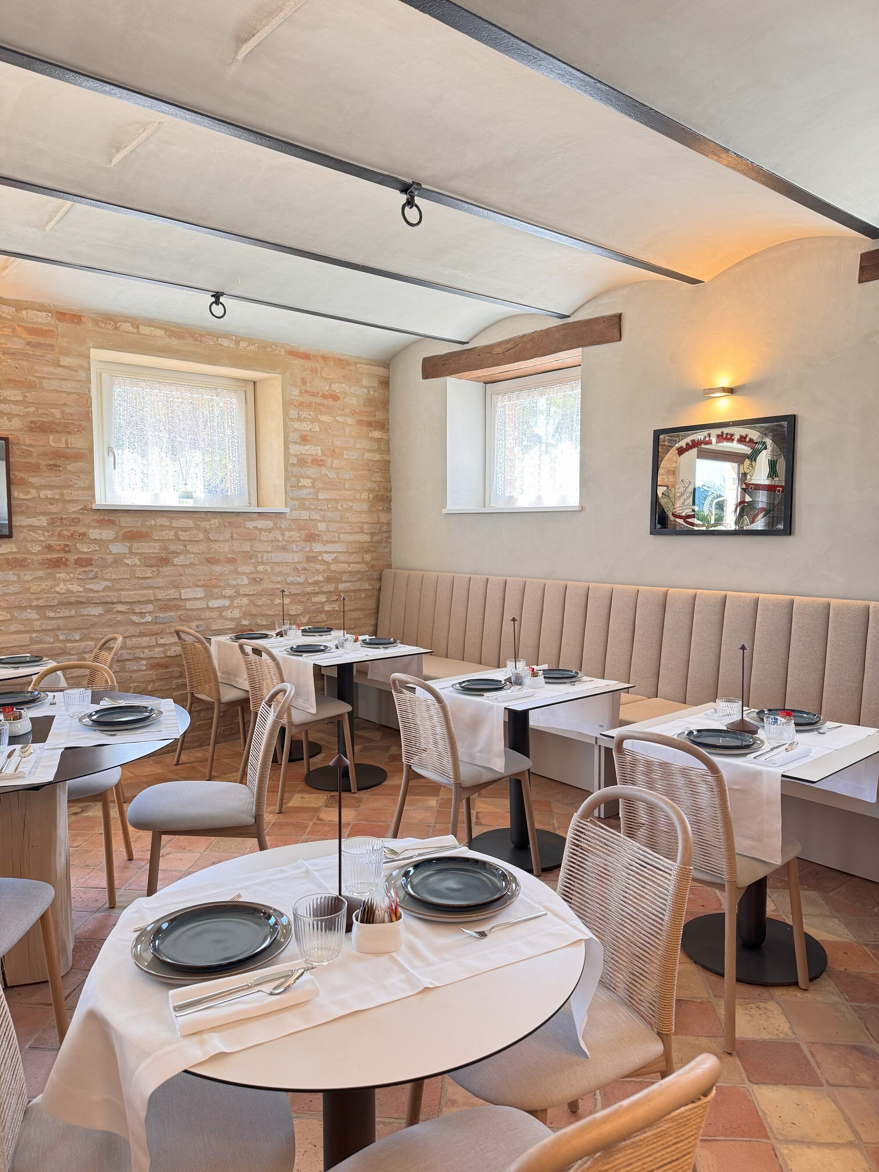 Ein Restaurant mit runden Tischen, gepolsterten Sitzecken und Backsteinwänden.