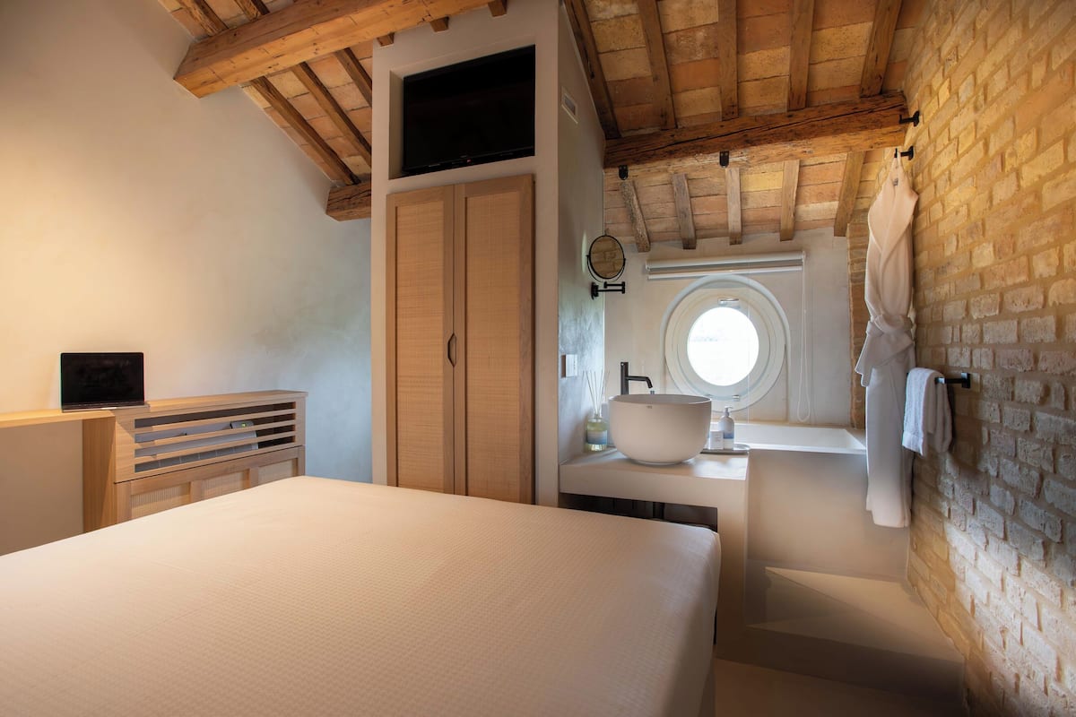 Un dormitorio con cama, armario de madera y baño con lavamanos y ventana.
