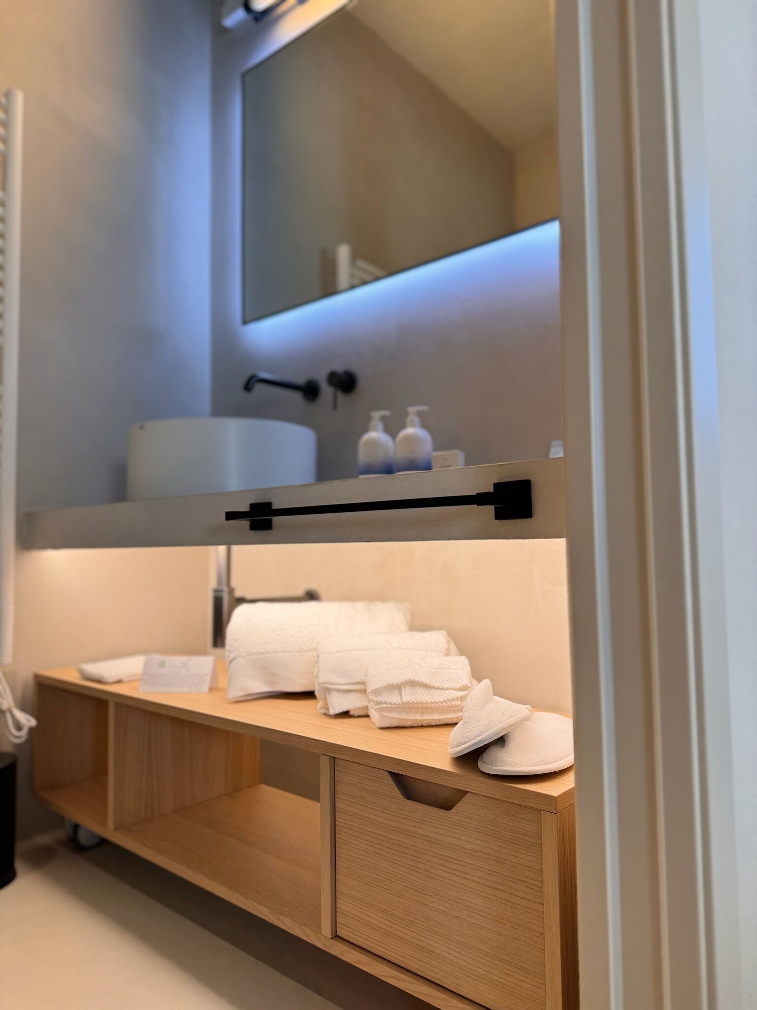 A modern bathroom with a wooden vanity, a mirror, and a shelf with toiletries.