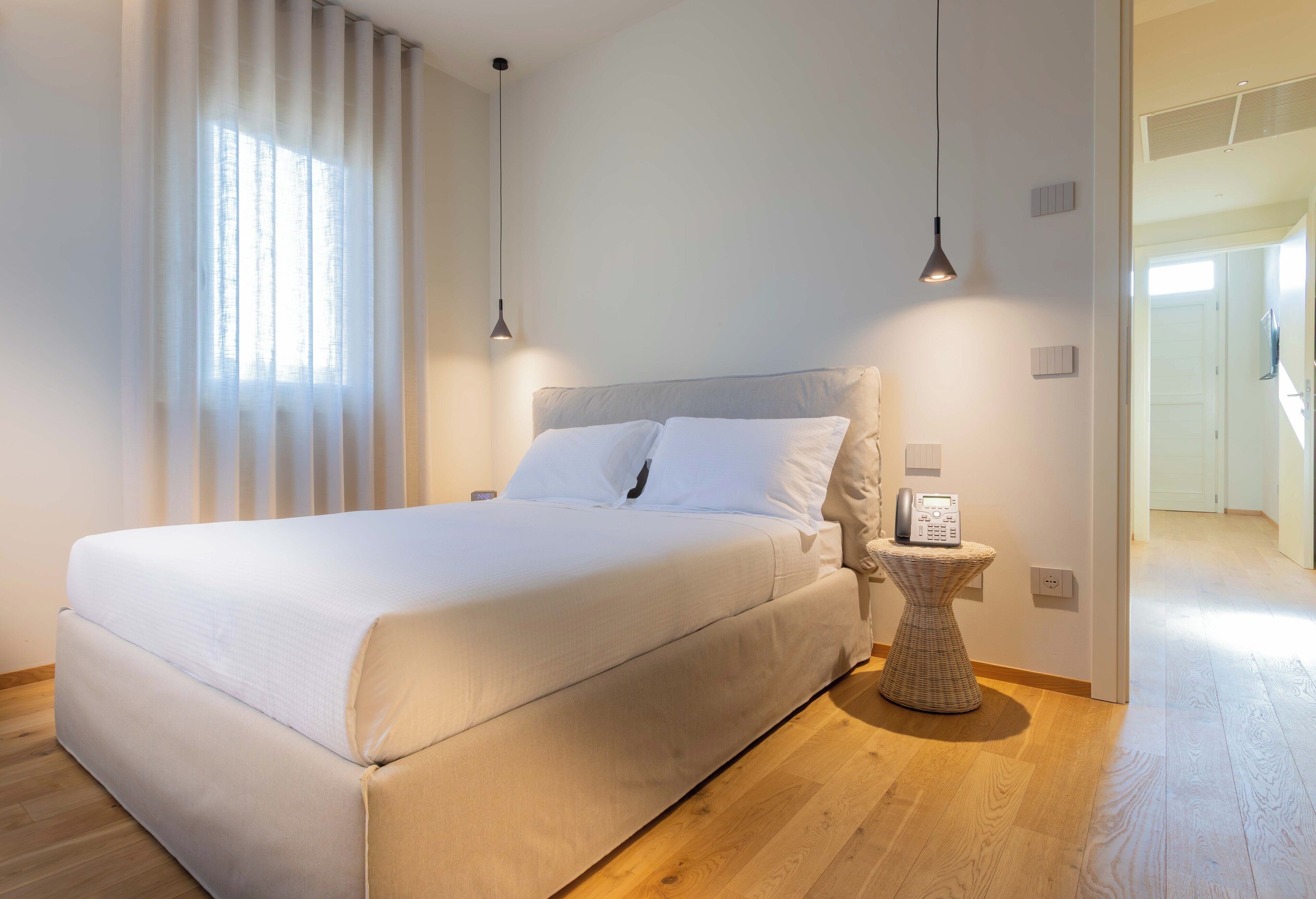 A modern bedroom with a large bed, a bedside table with a phone, and a view of a hallway.