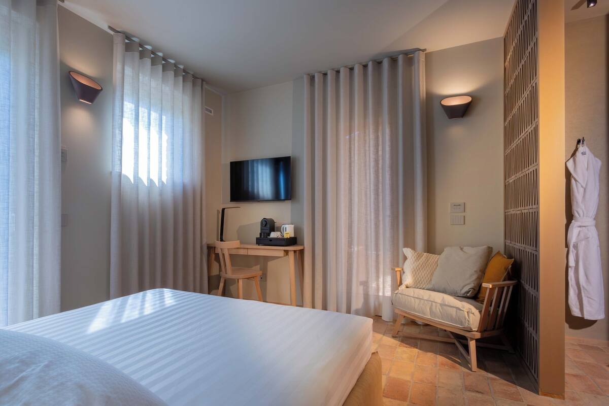 Habitación de hotel con cama, escritorio con televisor de pantalla plana, silla y bata colgada en la pared.