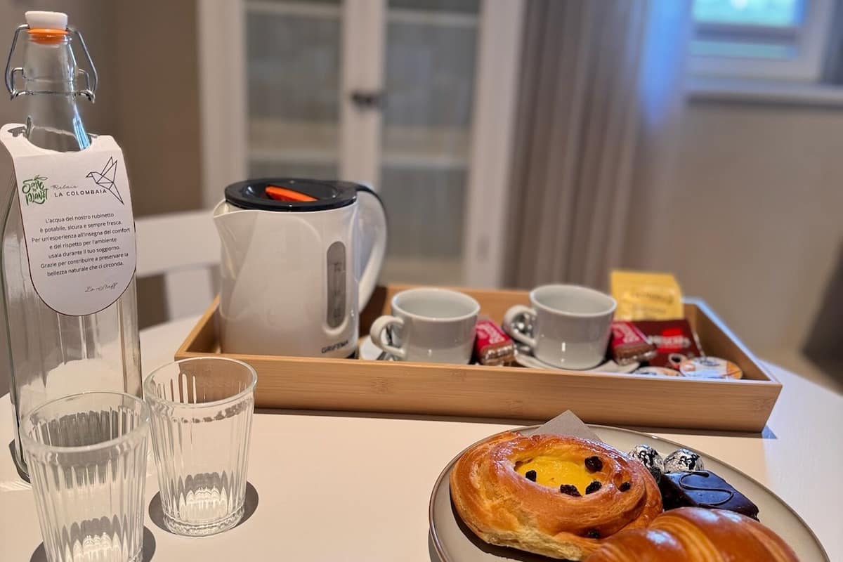 Una bandeja de desayuno con croissants, una cafetera, tazas y una botella de agua sobre una mesa.
